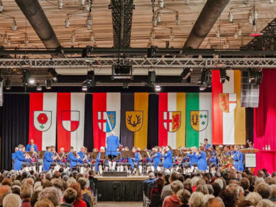 Konzert mit Orchester und Publikum. Wappen im Hintergrund. Musikveranstaltung.