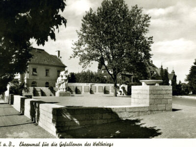 Schwarzweißfoto: Denkmal für die Gefallenen des Weltkriegs, Gebäude und Baum im Hintergrund.