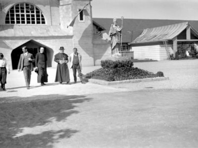 Historisches Foto: Gruppe von Personen vor Kirche mit Statue. Schwarz-Weiß-Aufnahme.